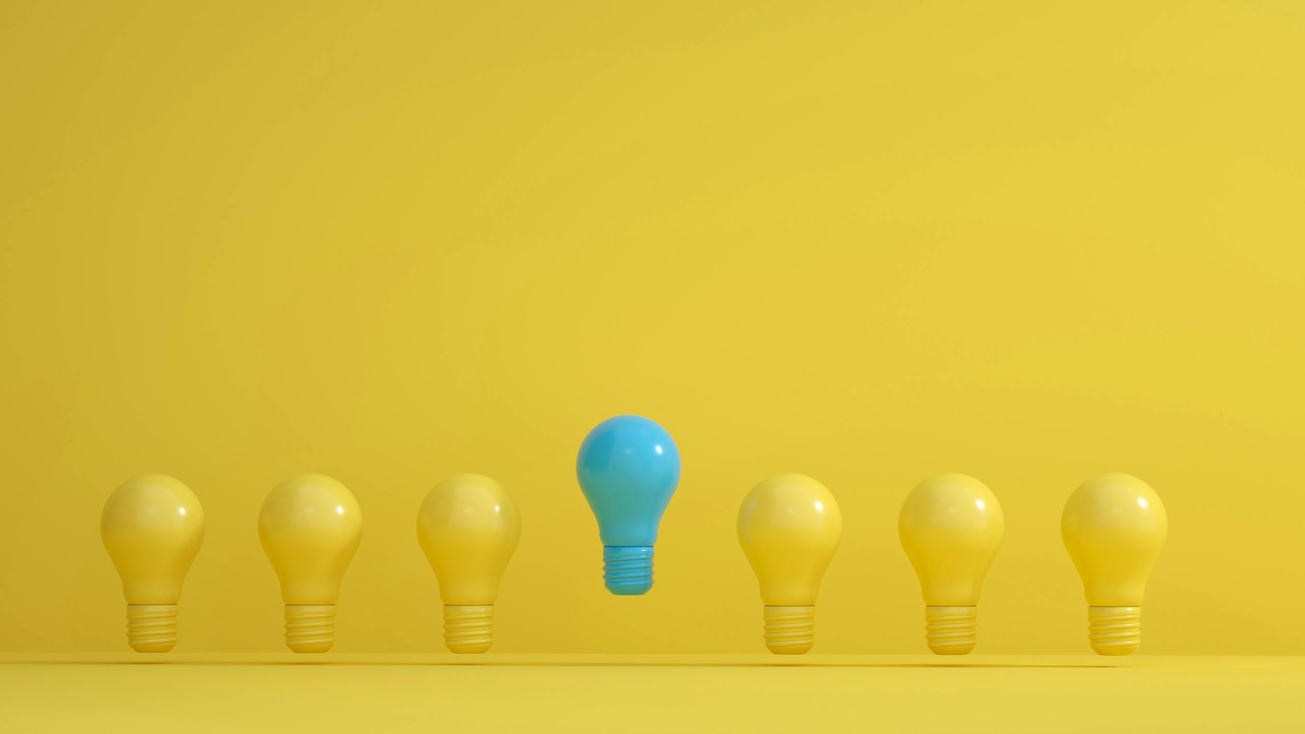 Une ampoule bleue se détache parmi plusieurs ampoules jaunes sur un fond jaune.