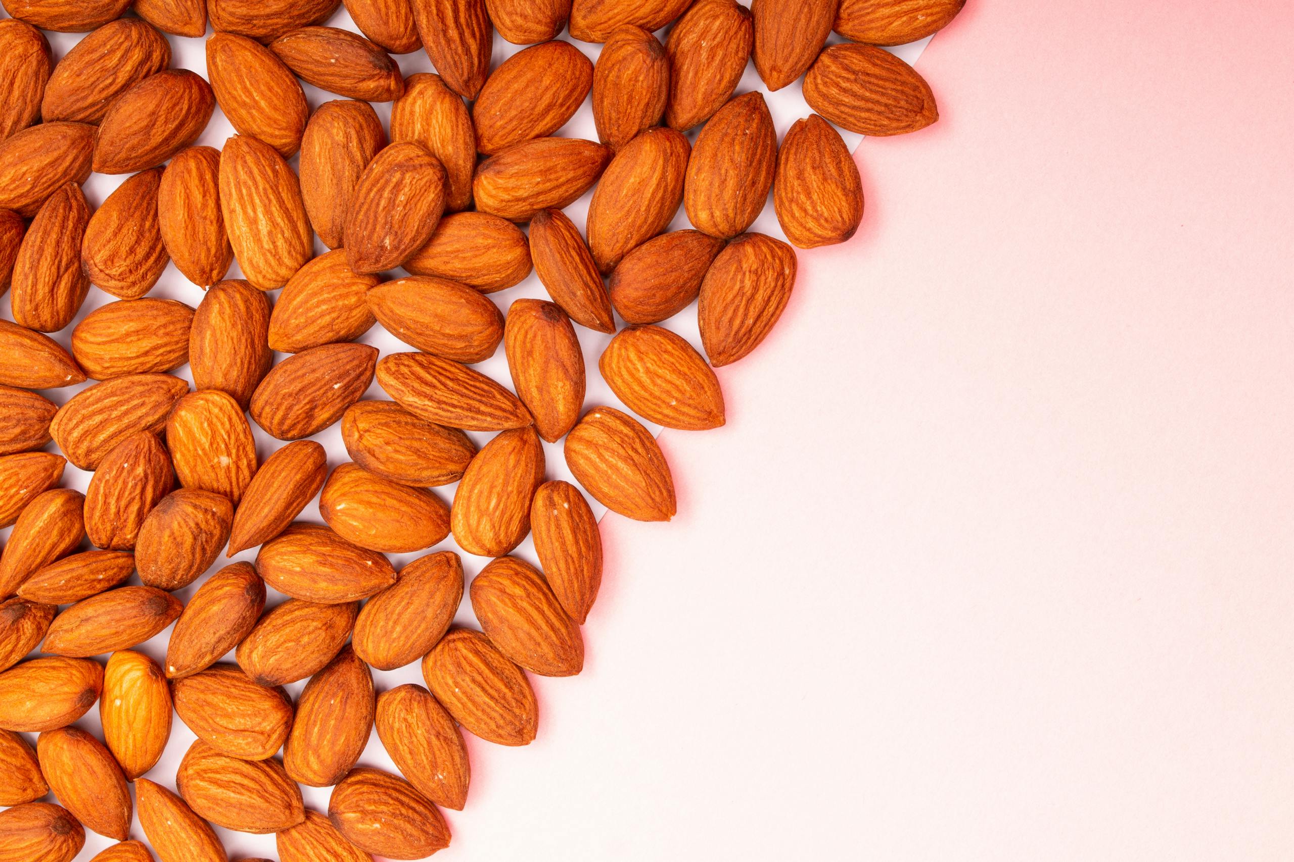 Des amandes bio disposées sur une surface rose pastel.