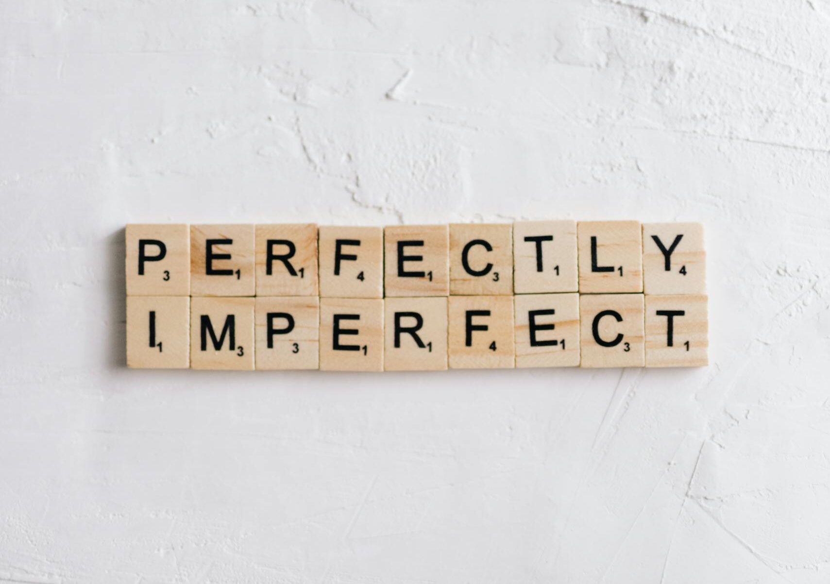Des lettres de Scrabble sur un fond blanc composent l'expression « Perfectly Imperfect ».